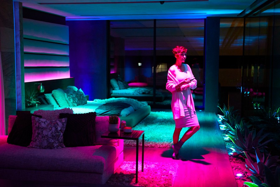 A woman in a bedroom with LED lights illuminated in shades of greens, blues, purples, and pinks.