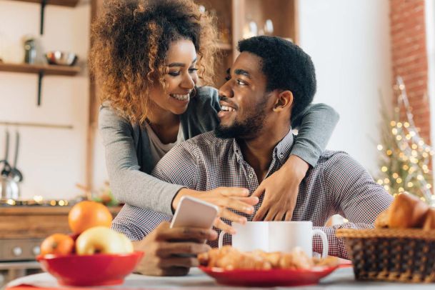 Woman wrapping arms around man holding phone